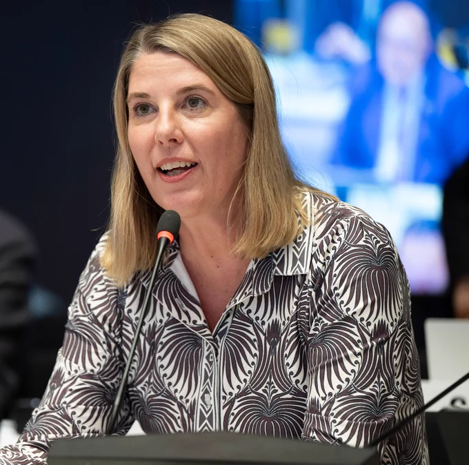 A woman in a patterned shirts speaks into a microphone at what looks to be a conference setting