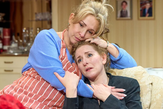 Two actresses console each other on a sofa on an onstage living room set