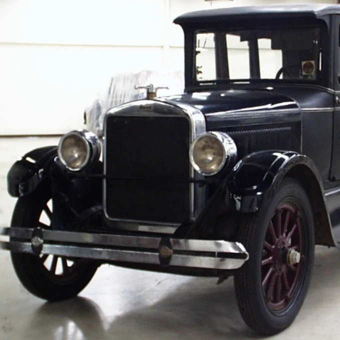 Vue avant d'une voiture vintage noire avec des phares ronds et une calandre chromée dans un garage.