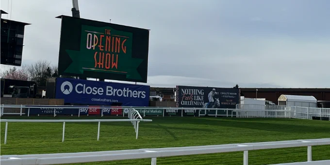 Racecourse scene with green turf, white railings and a large screen reading ‘The Opening Show’, with Close Brothers branding along the track.
