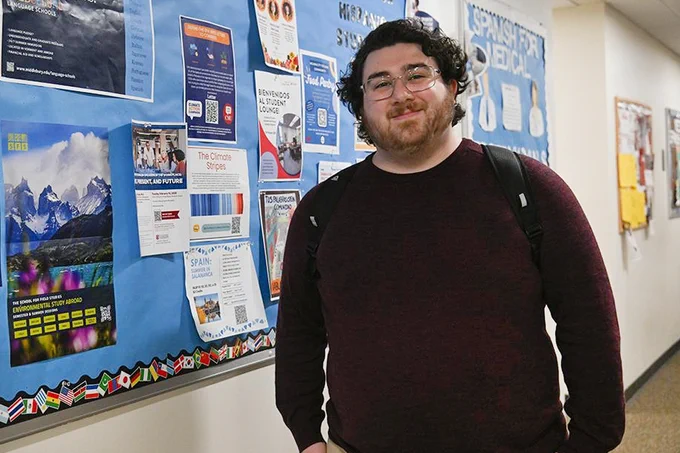 Nick Freilino stands in a hallway in College Hall. There is a billboard with posters on it at left.

