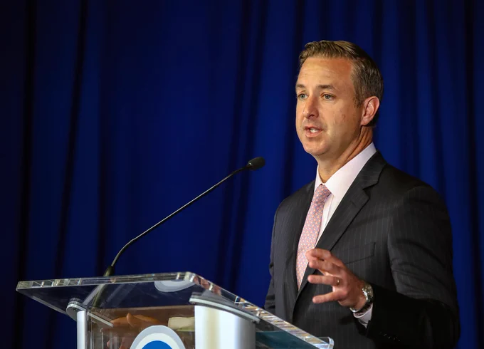 Pat Lyons delivering a speech behind a podium with a microphone, dressed in formal attire.