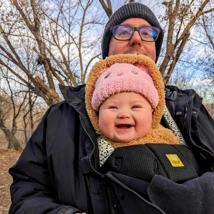 Baby smiling in front of dad Tim wearing a cute pink hat in a park during winter