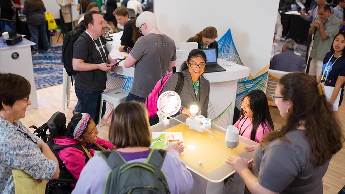 Several adults and smiling children interact with innovative technology at the C S U N Assistive Technology Conference Exhibit Hall.