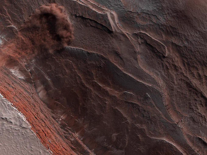 A top-down view of an avalanche plunging down a cliff. Reddish dust is kicked up into the air at top left. Credit: NASA/JPL-Caltech/University of Arizona