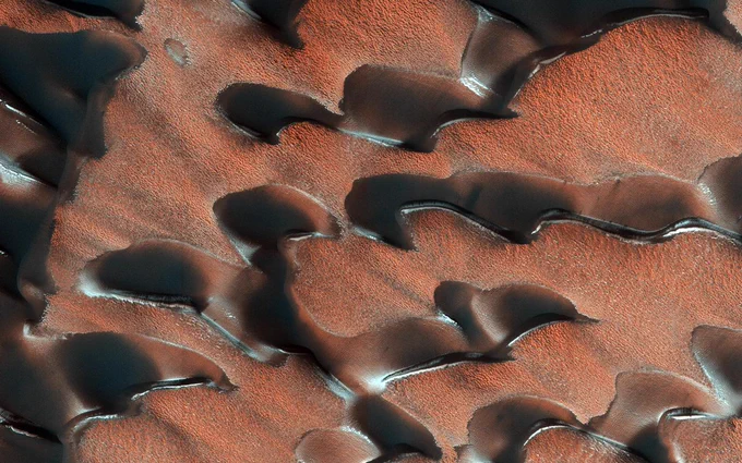 Sand dunes in the north polar regions of Mars have light coatings of pale orange dust partially covering the dark sand. White patches of seasonal dry ice line the edges of the dunes. Credit: NASA/JPL-Caltech/University of Arizona