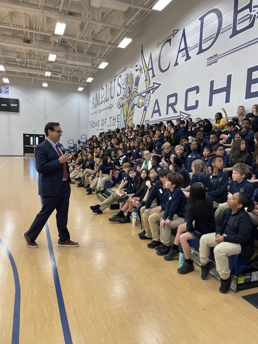 Secretary Aguilar speaks to students sitting in bleachers in school gymnasium