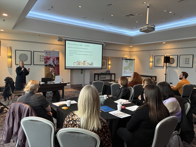 Sharon Donohoe is presenting at the front of a busy room full of housing professionals.