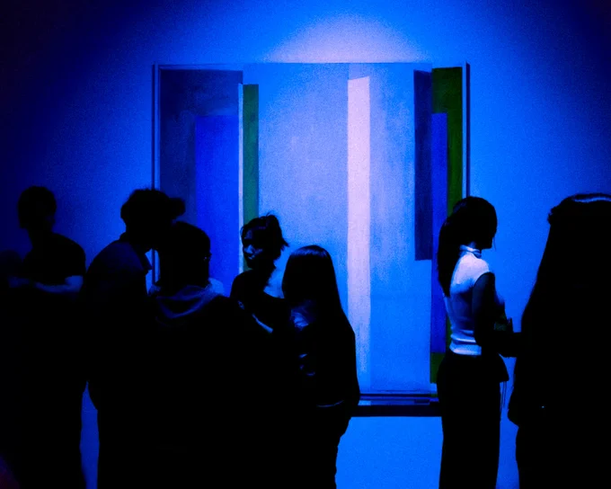silhouettes of a group of strangers centered against a large abstract painting comprised of vertical bars. deep royal blue tones and monochromatic in nature.