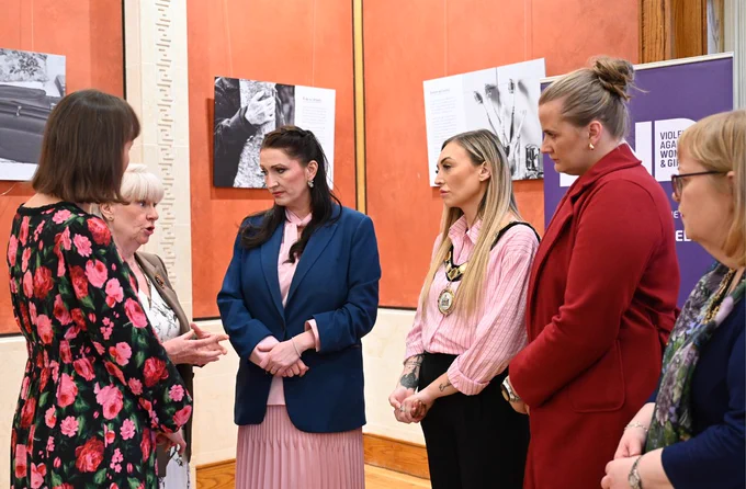 Image of six people standing talking  – pictured left to right are: Kathryn Torney, exhibition creator and journalist, Gillian Creevy, CEO Women’s Aid Antrim, Ballymena, Carrickfergus, Larne, and Newtownabbey, deputy First Minister Emma Little-Pengelly, Mayor of Antrim and Newtownabbey Borough Council, Leah Kirkpatrick, Junior Minister Aisling Reilly and Deputy Mayor of Antrim and Newtownabbey Borough Council, Julie Gilmour.