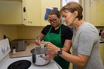 A nutrition agent helps someone prepare a meal at a stove. 
