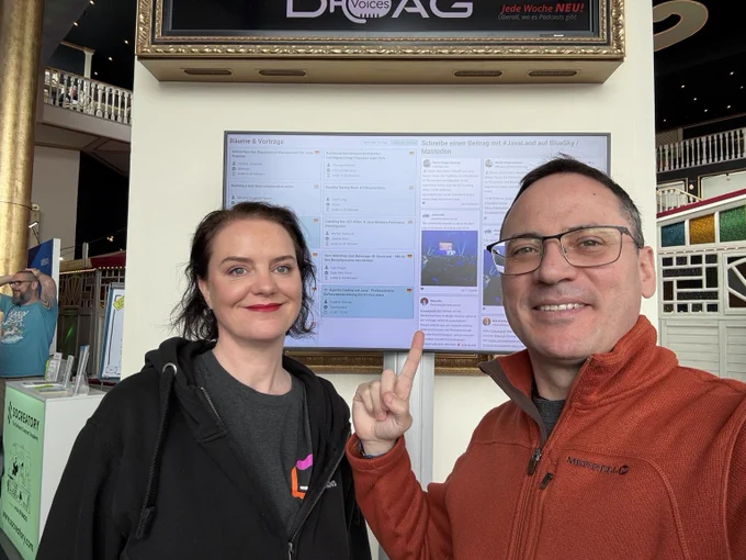 Marit van Dijk and Andres Almiray in front of a screen showing the JavaLand program and social media feed. Andres is pointing at the feed.