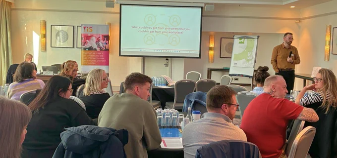 Pedro Cameron standing at the front of of a busy room, facilitating a discussion about peer support.