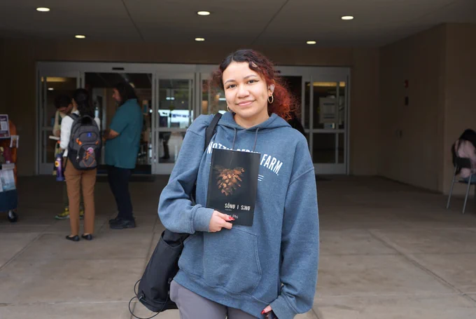 Person stands holding a book in front of the library entrance