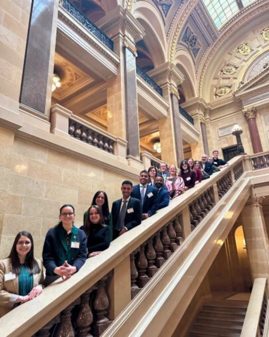 Group of students and faculty pose for a photo on a staircase at the Wisconsin State Capitol during the Research in the Rotunda Event.
