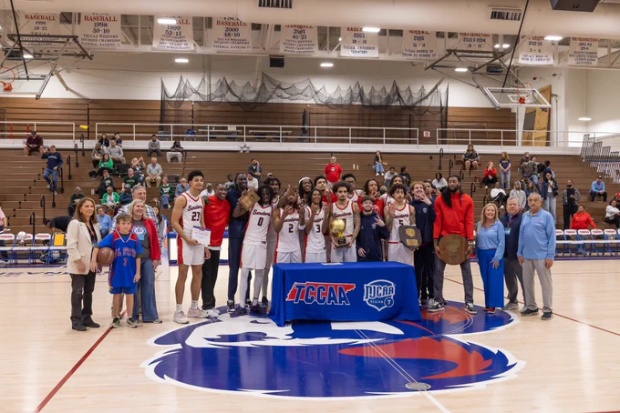 Image of the men’s tournament winners, Walters State Community College, on the basketball court smiling and holding the trophy.