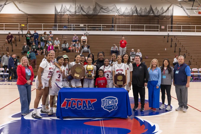 Image of the women’s tournament winners, Walters State Community College, on the basketball court smiling and holding the trophy.