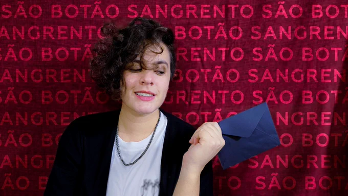 
Fai, olhando meio de lado, por cima do ombro. Ele usa uma camiseta branca e um cardigã preto por cima. Com a mão esquerda, ele segura um envelope preto muito suspeito... O fundo atrás é vermelho e tem escrito SÃO BOTÃO SANGRENTO várias vezes...