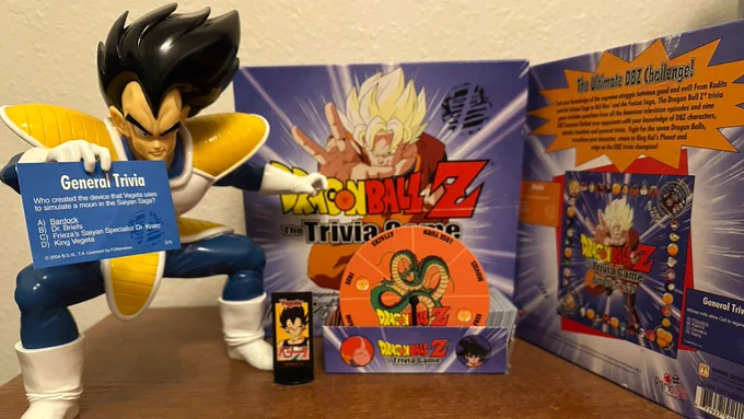 Vegeta holding a trivia card. Posed in front of the "Dragon Ball Z - The Trivia Game" released in 2004 by Parklife. The box and its contents (game pieces, spinner wheel, and trivia cards) are displayed next to each other.