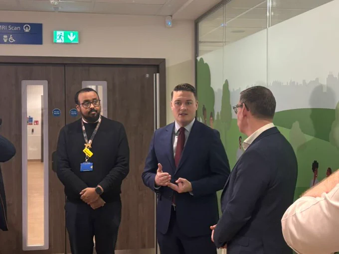 Wes Streeting in a suit speaking with colleagues in the CDC corridor
