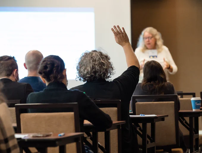 Attendees sit at tables during a Pennsylvania Legal Aid Network Statewide Training Conference session while one participant raises a hand to ask a question during a panel discussion.