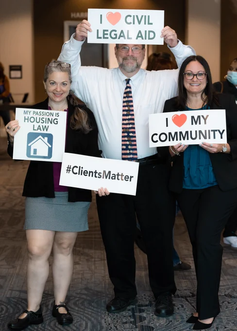 Three attendees at the Pennsylvania Legal Aid Network Statewide Training Conference pose together holding signs that read “I ♥ Civil Legal Aid,” “I ♥ My Community,” “My Passion Is Housing Law,” and “#ClientsMatter.”