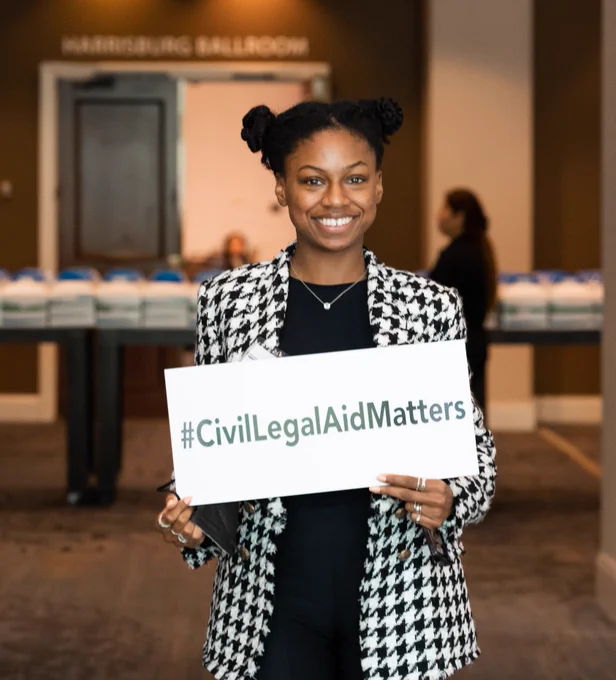 A woman smiles while holding a sign that reads “#CivilLegalAidMatters” during the Pennsylvania Legal Aid Network Statewide Training Conference.