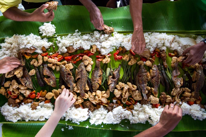 Six hands eat blue foods spread out in a beautiful display on a green leaf.
