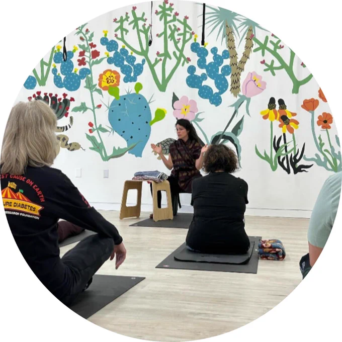 A group of people sitting on yoga mats listening to an instructor.