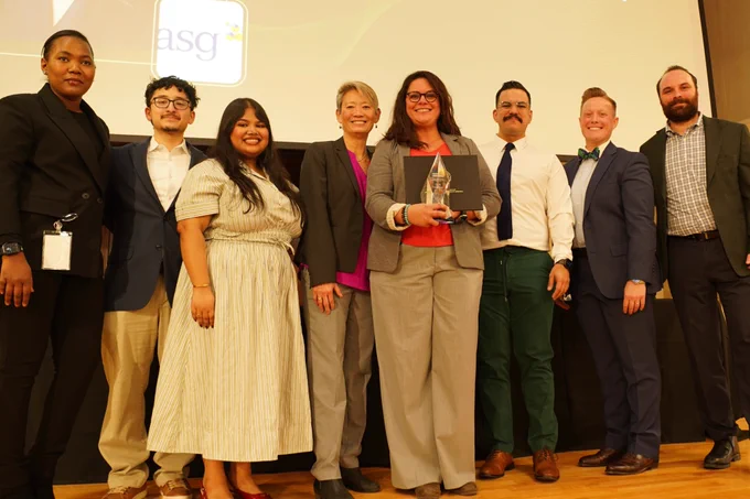 Josiane Martinez, a Latina woman with shoulder-length dark hair wearing a grey blazer and grey pants. She's with a multicultural group of teammates and Susu Wong, the Board Chair, an Asian woman with short blonde hair, and Alexandria Eberhadt, a woman with short red hair.