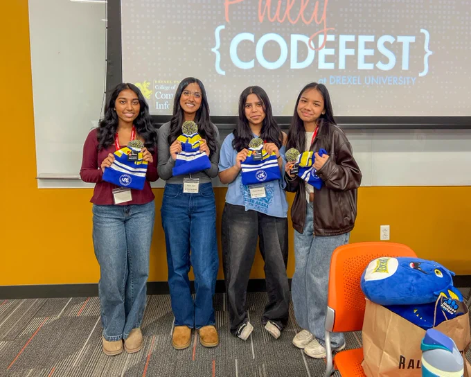 Four participants standing in front of a Philly Codefest presentation screen, each holding event swag bags and medals.