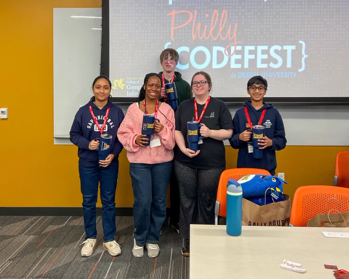 Five participants stand in front of a Philly CodeFest presentation screen holding awards and wearing event lanyards.
