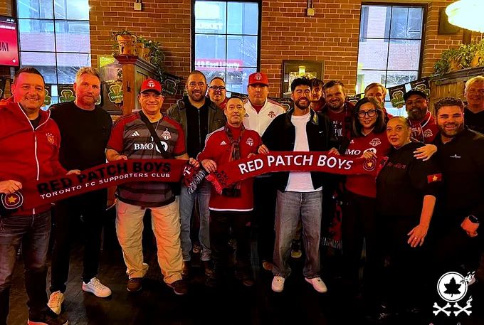 A group of Red Patch Boys members standing with scarves on display with various TFC personalities including Jimmy Brennan and Jonathan Osorio at the 2026 TFC Supporters Forum at Brazen Head. Red Patch 20-year watermark logo in bottom corner.