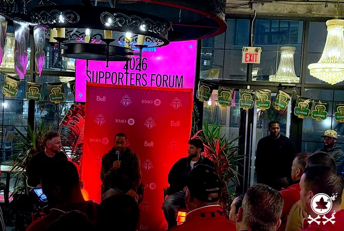 Various TFC players and coaches on stage for a panel at the Toronto FC 2026 Supporters Forum in front of a pink/red glowing backdrop. RPB 20-year anniversary logo watermark in bottom corner.
