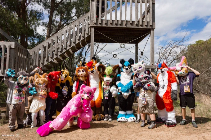 Several fursuiters standing outside in front of a tower viewing platform in a park.
