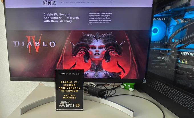 The GAConf Award 2025, a glass plaque with dark bacground and white and golden text. The text reads "Best Journalism Diablo IV: Second Anniversary Interview Antonio Martínez". Behind the trophy, a monitor shows the article on the website Game Accessibility Nexus. A gaming PC with blue RGB lights completes the scene.
