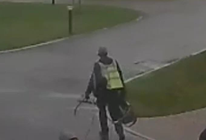a cctv image of a man in a cap carrying a bag and cable
