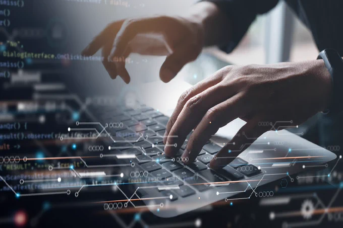 Close-up of hands typing on a laptop keyboard with digital code and data overlays representing programming activity.