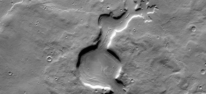 A landscape on Mars, seen from above, with a few small craters and a channel crossing the scene vertically through the center of the frame.