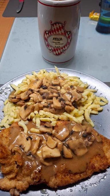 Jägerschnitzel mit Spätzle. Vor meinem Teller steht ein kleiner Steingukrug mit Radler. 