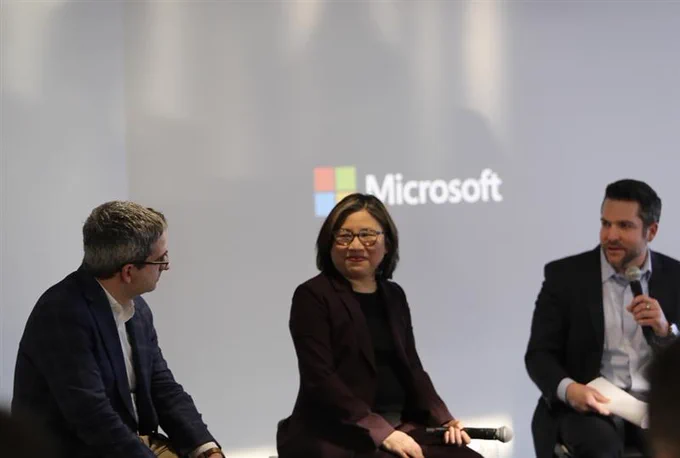 Oren Cass, Portia Wu and Gerry Petrella sit at the front of a room on a panel with the Microsoft logo in the background. Gerry is holding a microphone. 
