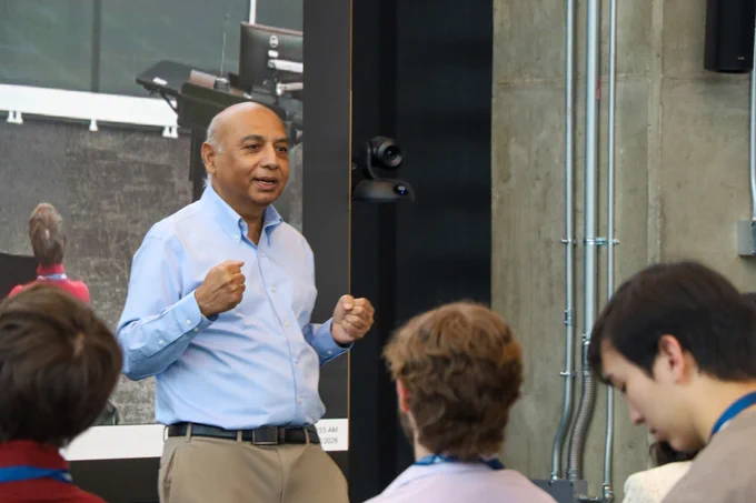 A man speaks to a crowded room of students.