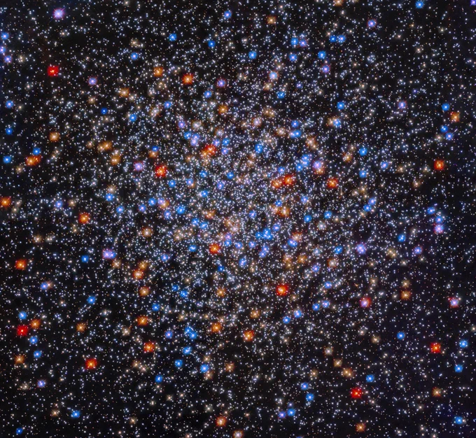 A colorful grouping of red, yellow, orange, blue, and white stars sits at image center. The stars appear close together at image center and appear less dense as you move outward.