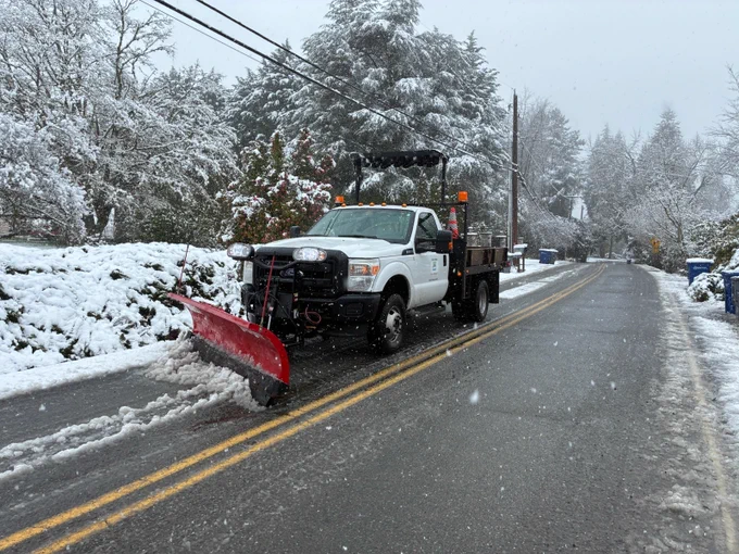 A City of Bothell Public Works truck with a snowplow blade attached at the front pushes snow out of the roadway.