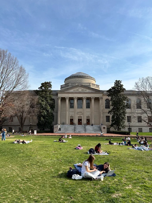 Photo of the exterior of Wilson Library, with students sitting in the quad in the foreground. 