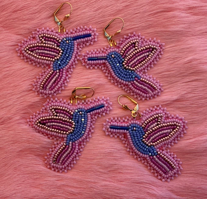 Two pairs of flat stitched beaded hummingbird earrings in a pink and blue design. Laying on pink rabbit fur.
