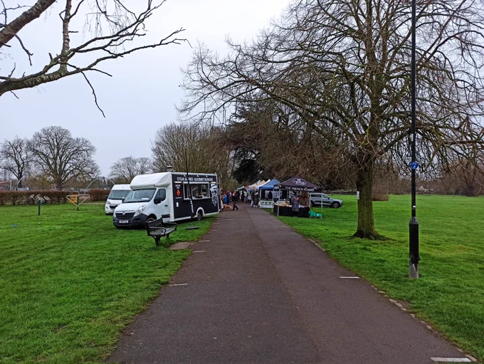 The cycling route through Beddington Park has been taken over by a market with vehicles and stalls set up either side of the wide hard surfaced path with people browsing stalls. No approach warning has been placed on the west side of the market 