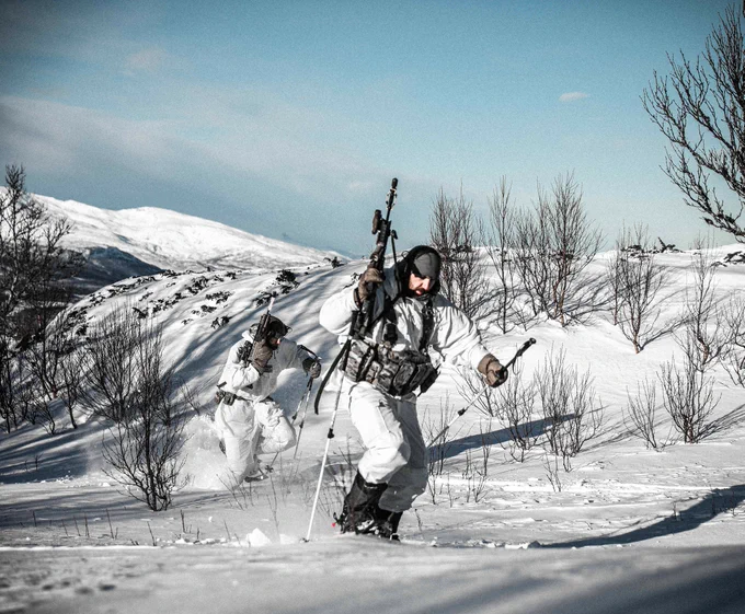Members of the RAF Regiment using ski poles to traverse a snowy slope.