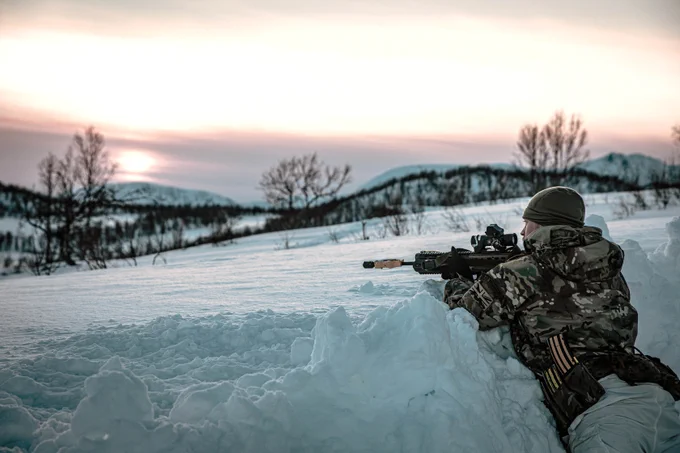 A member of the RAF Regiment with a rifle laying down in the snow.