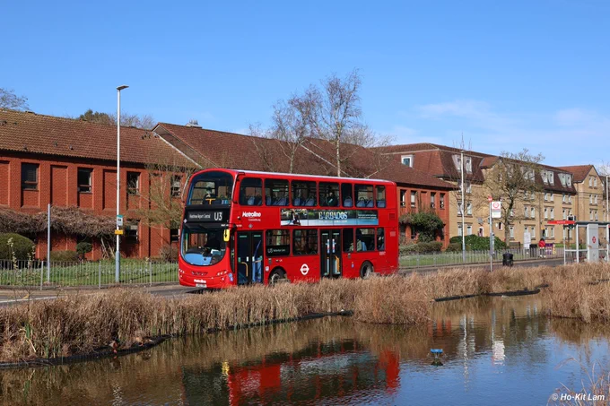 Metroline VW1381 (LK62DRV) is a red Volvo B9TL Gemini 2 and is pictured heading to Heathrow Airport Central on route U3. 

In the picture there is a pond with the reflection on the bus reflecting on the water. The bus is in the middle of the picture heading to the left of the screen. 